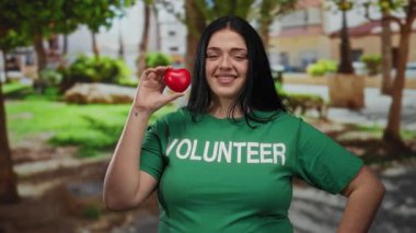 Parkta elinde kalp sembolü tutan yeşil gönüllü gömleği olan, toplum ruhunu sergileyen, kilolu, kıvrımlı bir kadın..