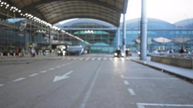 Modern bir mimari ortamda yoğun seyahat aktivitesi gösteren odakları kesilmiş insan ve araçların bulunduğu bir açık hava terminalinin bulanık görüntüsü.