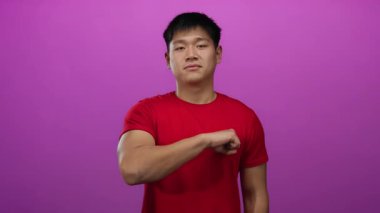 Kırmızı tişörtlü genç Çinli adam güvenlik ve güç iletmek için izole edilmiş pembe arka plana doğru yumruğunu uzattı..