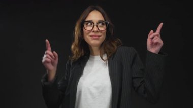 Siyah arka planda yalnız dans eden, gözlüklü, şık ceketli, hareketli ve neşeli bir gülüşü olan bir kadın..