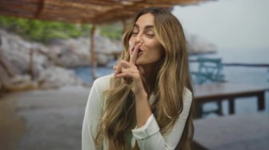 Kadın deniz kenarındaki kafede sessizlik için parmaklarını dudaklarına uzatıyor..