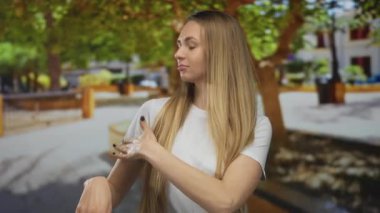 Uzun saçlı bir kadın, güneşli bir parkta dikilip arka planda ağaçlar ve şehir manzarası olan huzurlu bir açık hava ortamının tadını çıkarıyor..