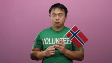 Genç Asyalı adam Norveç bayrağını tutarken pembe arka planda hareketler yapıyor..