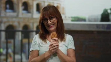 Roma 'daki sembolik Roma stadyumunun arka planına karşı elinde bozuk parayla gülümseyen İspanyol kadın, tarihi bir şehir ortamında canlı bir enerji sergiliyor..