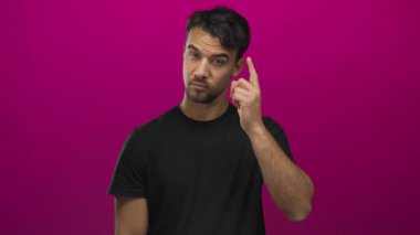 Siyah tişörtlü genç İspanyol adam canlı pembe arka plana karşı düşünceli bir şekilde hareket eder canlı bir kontrast yaratır ve düşünceli bir ifade yaratır.