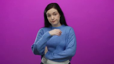 Parlak pembe bir arka plana karşı duran, mavi bir kazak giyen, kumral saçlı, çapraz kolları ve düşünceli bakışlarıyla tefekkür eden bir kadın..