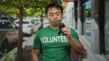 Şehir caddesinde elinde siyah kurdele tutan genç adam, arka planda ağaçlar ve arabalarla gönüllü yas tutarken kasvetli ruh halini gösteriyor..