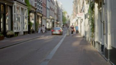 Amsterdam 'daki bulanık yayalar ve güneşli gökyüzü altındaki arabalarla bulanık sokak manzarası Hollanda' nın kentsel atmosferini yumuşak Bokeh etkisi altında yakalıyor..