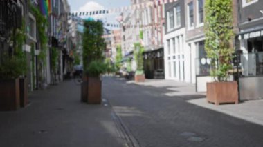 Hollanda 'da sakin bir günde güneşli gökyüzü altında canlı bayraklar ve saksılarla bulanık sokak manzarası rüya etkisi yaratmak için dağıtıldı..