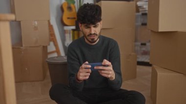 Genç adam yeni bir dairede yerde oturuyor. Etrafı akıllı telefonla oynayan kutularla çevrili. Arka planda gitarla rahatlamış bir anı gösteriyor..