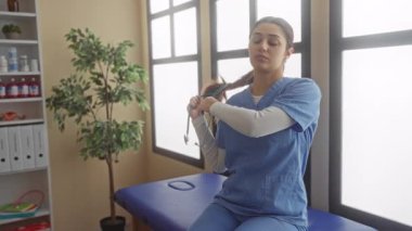 Mavi önlüklü kadın steteskopu kaldırıyor sonra da büyük pencereli ve yakındaki saksı bitkisi olan parlak, aydınlık bir klinik odasına tıbbi rapor yazıyor..