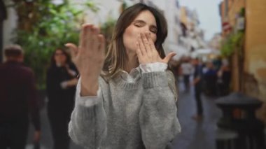 Hareketli bir şehir caddesinde hayat dolu bir atmosferi olan ve arka planda bulanık yayalar olan bir kadın, neşeli ve dinamik bir açık hava sahnesi yakalıyor..