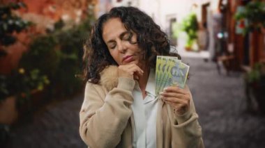 Bir şehir caddesinde elinde Romanya banknotları tutan orta yaşlı bir kadın dinginlik ve tefekkür ifadesiyle bir anlık finansal yansımayı yakalıyor..