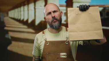 Kahverengi önlüklü kel bir adam eski üniversitede elinde kesekâğıdıyla geziyor. Kemerleri ve kendine güveni olan özel bir eğitim ortamı sergiliyor..