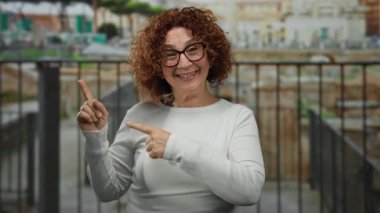 Antik Roma harabelerinin önünde gülümseyen bir kadın iki eliyle dışarıyı işaret ederek canlı bir şehirde tarihi bir cazibe ve kültür mirası sergiliyor..