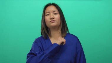 Mavi gömlekli bir kadın, yeşil arka planda poz veriyor, kendine güveni tam, izole bir ortamda, odaklanmış stüdyo ortamında genç ve rahat bir ortam yaratıyor..