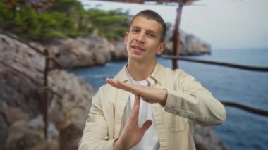 Sahilde mola veren bir adam arka planda kayalık kıyı, ağaçlar ve mavi denizle açık deniz ortamında mola veriyor..