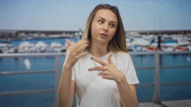 Arka planda teknelerle coşkuyla el kol hareketi yapan ve güneşli bir günde rıhtım kenarında seyahat eden bir kadın.