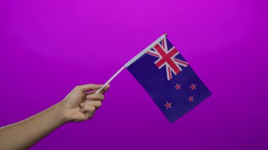 Pembe arka planda yeni Zelanda bayrağı taşıyan bir adam, ulusal gurur ve kimlik gösterisi yapıyor..