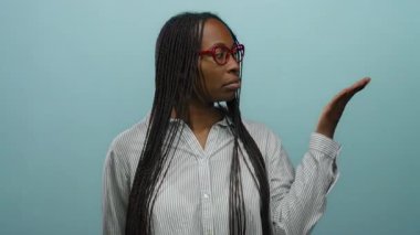 İzole edilmiş stüdyo ortamında mavi duvara karşı el kol hareketi yapan bir kadın..