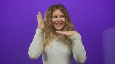 Stüdyo resminde elleri kullanan ve mor arka planda gülümseyen genç sarışın bir model olarak resmedilen bir kadın..