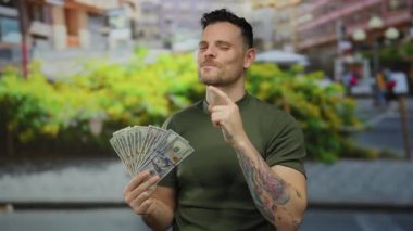 Latin kökenli genç adam şehir sokaklarında bize dolar tutuyor. Düşünceli bir yüz ifadesi var. Parmak hareketiyle altı çizili..