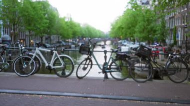 Bisikletler, arka planda bulanık ağaçlar ve binalar bulunan ve Hollanda 'nın özünü yumuşak bir bokeh tarzında yakalayan bir kanal boyunca dizilmiş..