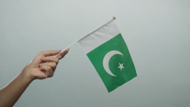 Pakistan bayrağını arka planda tutan adam, ulusal gurur ve kimliğin canlı bir temsilini sergiliyor, izole edilmiş ve eli sıkıca kavramaya odaklanmış..