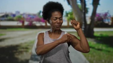 Neşeli bir kadın parkın dışında kaslarını esnetiyor. Güneşli bir günde güçlü ve kendine güvenli bir hava sergiliyor..