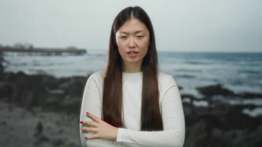 Kumsalda duran, uzun saçlı, duygularını ifade eden, beyaz gömlek giyen, açık hava, genç, yetişkin, Asyalı, güzel bir kadın..