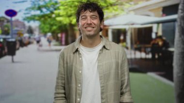 Açık havada, yeşillik dolu ve güneşli bir günde arka planda insanları heyecanlandıran canlı bir sokakta öpüşen bir adam..