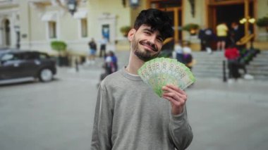 Elinde Rus rublesi olan bir adam şehir caddesinde arka planda insanlar ve arabalarla gülümsüyor para ve kaygısız ruh hali sergiliyor..