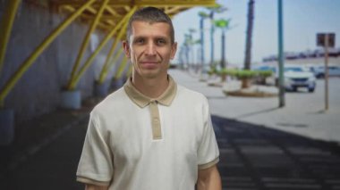 Kapalı gözlü bir adam, günışığında kaldırımı saran sarı kirişli ve palmiye ağaçlarıyla modern sokak yapısının yanında duruyor..