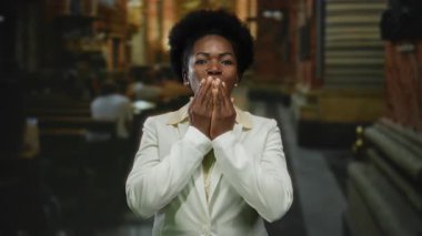 Kilisedeki kamerayı öpen, arka planı bulanık beyaz takım elbiseli, kapalı mekanı aydınlatan bir kadın..