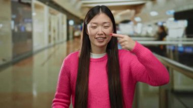 Modern alışveriş merkezinin içinde renkli süveter giyen bir kadın alışveriş merkezinde neşeli bir ifade sergiliyor ve canlı bir iç mekan atmosferi yakalıyor..