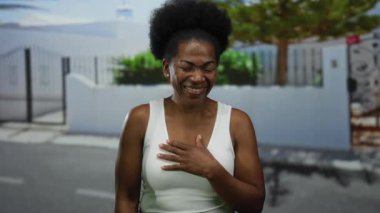 Şehrin arka planında ağaçlar ve beyaz çitlerle gülümseyen bir kadın, elini göğsüne koyup sevinçten havalara uçuyor..