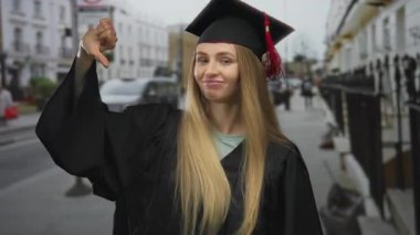 Mezuniyet elbisesi giymiş bir kadın şehir caddesinde duruyor. Onaylıyor ve onaylamıyor. Şehir ortamında karışık duyguları simgeliyor..