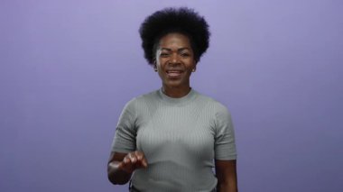 Mor arka planda selamlaşan kadın, şakacı bir şekilde dilini uzatıyor ve göz kırpıyor; genç, neşeli, Afrikalı, Amerikalı kadın sıcaklık ve dostluk saçıyor..