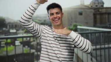 Roma harabelerinin önünde poz veren genç bir adam, gün boyunca açık havada gülümseyen, çizgili bir kazak giyen, kentsel bir ortamda enerjik ve çekici bir enerji sergileyen..