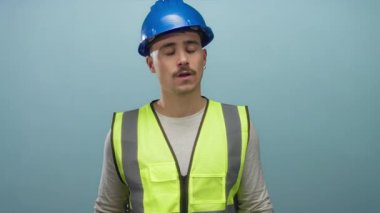 Yansıtıcı yelek giymiş genç İspanyol bir adam mavi arka plana karşı ingiliz anahtarı tutuyor. Kararlılık ve çalışmaya hazır olduğunu gösteriyor..