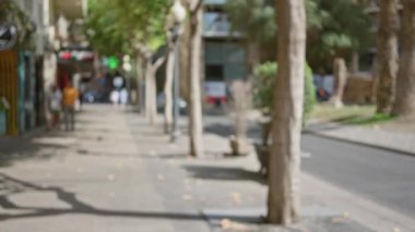 Güneşli bir günde ağaçların, insanların, arabaların, kaldırımların ve binaların bulunduğu bir şehir caddesinin bulanık görüntüsü Bokeh 'i ve odak dışında kalan unsurları gösteriyor.