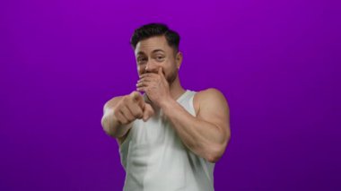 Sakallı genç adam soyutlanmış mor bir arka plana bakıp gülüyor beyaz bir gömlek giyiyor ve neşeli ve kaygısız bir tavır sergiliyor..