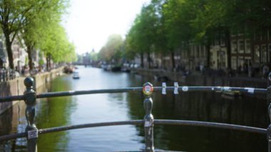 Amsterdam Kanalı 'nın bulanık manzarası. Odaklanmış arka plan, köprü rayı ve su altındaki yemyeşil ağaçları gösteriyor..