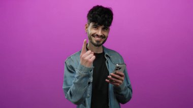 Akıllı telefonuyla gülümseyen genç adam izole edilmiş pembe arka planda kot ceket giyiyor.