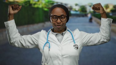 Beyaz önlüklü ve steteskop takmış bir kadın kenar mahallede güven içinde poz veriyor, mesleğinin gücünü ve gururunu gösteriyor..