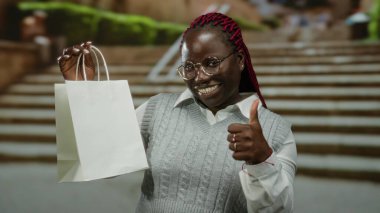 Alışveriş torbası tutan ve şehir merdivenlerinde baş parmağını sallayan bir kadın..