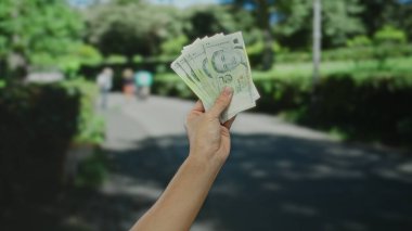 Güneşli bir caddede elinde Singapur doları tutan adam şehirde para ve açık hava aktivitelerini ön plana çıkarıyor..