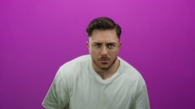 İzole edilmiş, pembe arka planı olan sakallı genç bir adam beyaz tişört giyiyor.