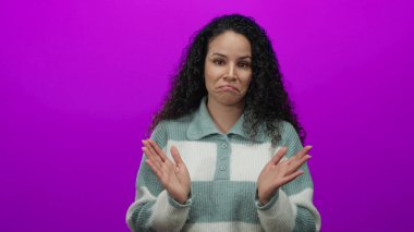 Kıvırcık saçlı bir kadın, izole edilmiş pembe bir duvara karşı duruyor. Sıradan bir kazakla ellerini çırpıyor. Arkaplanda nötr bir ifade sergiliyor.