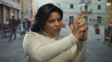 Bir kadın şehir sokaklarında eli silahlı bir jest yapıyor, kalabalık bir şehir zemininde tutumunu ifade ediyor..